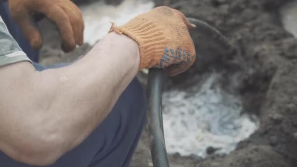 Close-up de mão masculina derramando água no poço de pouso. Agricultor caucasiano sênior irreconhecível em luvas de trabalho preparando solo de terra preta para plantio. Jardinagem, agricultura, agricultura . — Vídeo de Stock