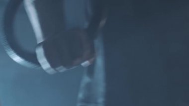 Kafkas sporcusunun, sisli halkalarla yüzüklerini çekiştirdiği yakın çekim elleri. İçerideki sisli spor salonunda atletik bir adamın çalışması. Spor, vücut geliştirme, sağlıklı yaşam tarzı..