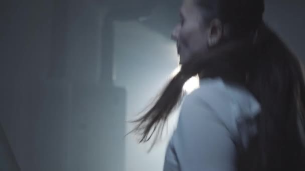 Side view close-up of brunette sportswoman jogging in backlight in misty fog. Portrait of sportive young Caucasian woman running on treadmill. Lifestyle, sport, athleticism. — Stock Video