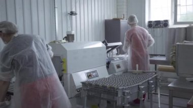 Fabrikadaki vakum makinesinde çalışan iki kadının arka plan görüntüsü. Yetişkin Kafkasyalı çalışanlar karantinadaki imalat tesisinde satılık gıda paketlerini paketliyorlar. Yaşam tarzı, üretim, üretim.