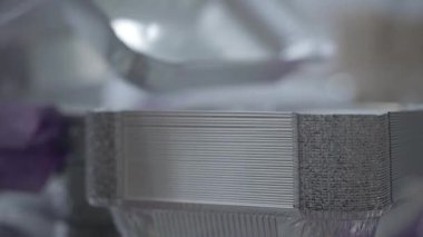 Yemek konteynırlarını sıralayan aşırı yakın çekim. Koruyucu eldivenli kadın eller fabrikada bitmiş ürünleri depoluyor. Tanımlanamayan bir uzman üretim hattında çalışıyor. İş, endüstri.