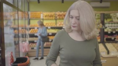 Son sınıf beyaz bir kadının marketteki buzdolabından ürün seçerken yakın plan portresi. Konsantre olmuş yetişkin bir kadın süpermarketten alışveriş yapıyor. Yaşam tarzı, temizlik, alışveriş. S-log 2.