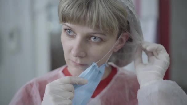 Retrato de cerca de una joven mujer caucásica poniéndose una máscara facial antes de trabajar en la cuarentena de Covid-19. Cara de trabajadora de fábrica seria en el sitio de producción. Industria, negocio, producción . — Vídeos de Stock