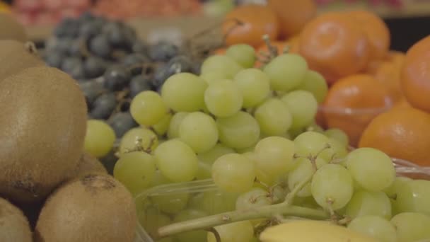 Close-up of fresh delicious green grapes, kiwi fruits and tangerines in grocery store. Tasty healthful food lying on the shelf of retail shop. Dieting, vitamin goods, healthy eating. S-log 2. — Stock Video