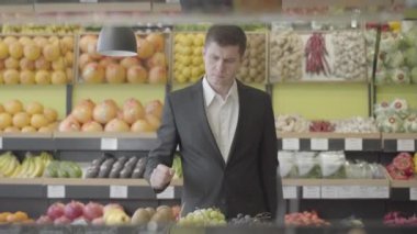 Marketteki en iyi limonu seçen konsantre beyaz adamın portresi. Zarif takım elbiseli kendine güvenen yetişkin bir adam markette sağlıklı narenciye meyvesi seçiyor. Vitamin yiyeceği, diyet, vejetaryenlik. Evet.