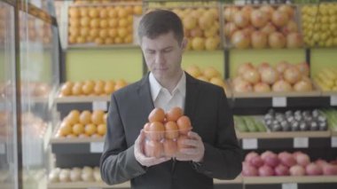 Mandalina kokusu alan ve kameraya gülümseyen mutlu erkek market müşterisinin portresi. Kafkasyalı yetişkin bir adam perakende dükkanında lezzetli vitamin sitrüslerini seçiyor. Yaşam tarzı, sağlıklı beslenme. S günlük kaydı