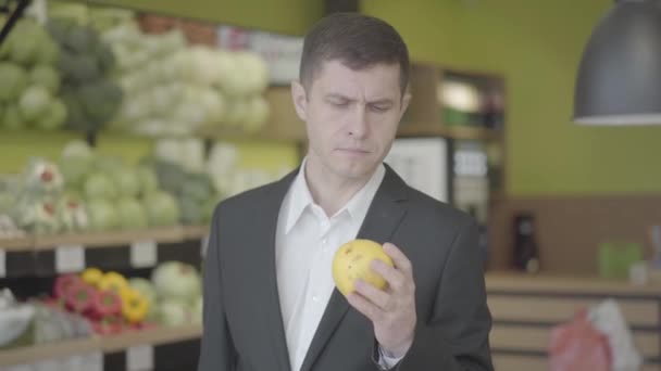 Portret van een zelfverzekerde serieuze man die peer selecteert in de supermarkt. Jonge blanke man die geel fruit te koop kiest in de supermarkt. Vitamine voedsel, gezond eten, levensstijl, vegetarisme. S-logboek 2. — Stockvideo