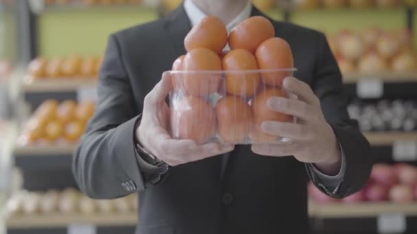 Homem caucasiano irreconhecível em terno cesta de alongamento de deliciosas tangerinas suculentas para a câmera. Mãos masculinas segurando saborosos frutos de laranja no supermercado. Dieta saudável, alimentos vitamínicos, dieta, estilo de vida. S — Vídeo de Stock