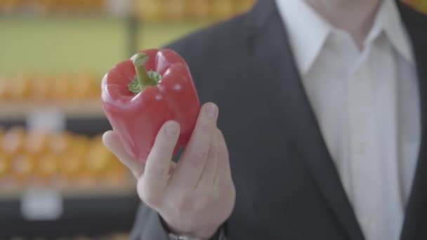 Close-up de mão branca masculina segurando pimentão vermelho fresco no supermercado. Homem irreconhecível mostrando vegetariano vegetal saudável na câmera. Alimentação saudável, vegetarianismo, estilo de vida, nutrição. S — Vídeo de Stock