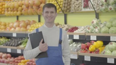 Markette poz veren esmer, beyaz bir adamın portresi. Dosyasına bakıp kameraya gülümseyen olumlu bir çalışan. Yaşam tarzı, meslek, ticaret. S-log 2.