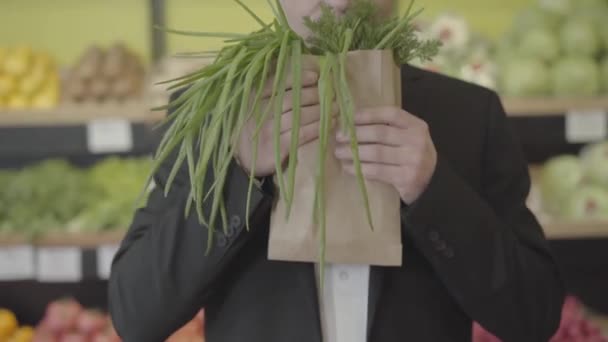 无法辨认的白人男子在纸袋里闻到了丁香和绿色洋葱的味道，并向相机伸出了一丛丛绿色的植物。未知的男性顾客在杂货店购买健康食品。S-log 2. — 图库视频影像