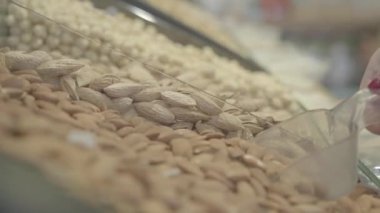 Market rafından sağlıklı fındıkları alan tanınmamış beyaz bir kadının eli. Süpermarkette çiğ badem toplayan tanınmamış kadın müşteri. Sağlıklı beslenme, yaşam tarzı, vejetaryenlik. S-log 2.