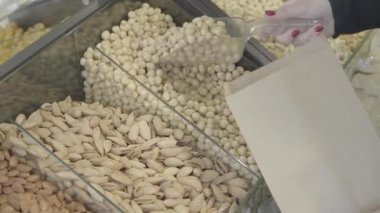 Beyaz bir kadın, kağıt torbada çiğ organik macadamia topluyor. Bilinmeyen bir bayan müşteri market rafından sağlıklı fındık alıyor. Vejetaryenlik, sağlıklı beslenme, yaşam tarzı. S-log 2.