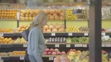 Bakkalda sıra sıra yürüyen ve sohbet eden iki sarışın Kafkasyalı ev kadınının yan görüntüsü. Kendine güvenen ciddi kadınlar süpermarkette sağlıklı yiyecekler seçiyor. Yaşam tarzı, tüketim, alım. S-log 2.
