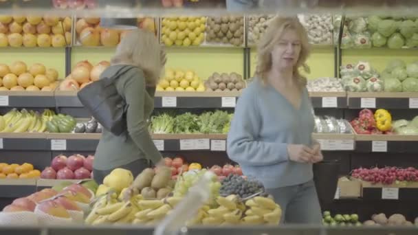 Retrato de dos mujeres caucásicas mayores caminando entre filas en la tienda de comestibles y hablando. Amas de casa adultas discutiendo compras en tienda minorista. Consumismo, estilo de vida, compras, cocina. S-log 2 . — Vídeos de Stock