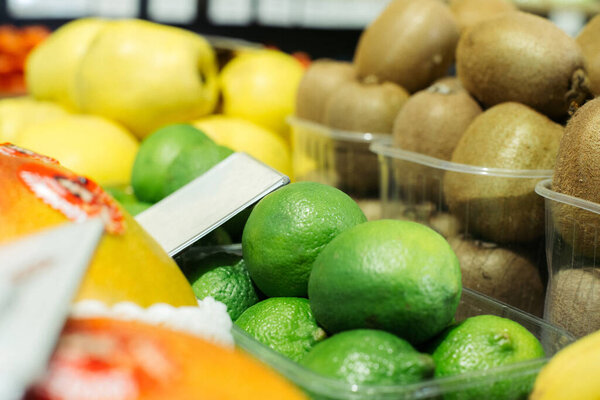 Green limes on shelf with blurred kiwi and pears at the background. Healthy vitamin eating, organic food, fruits in grocery.. Stock Picture