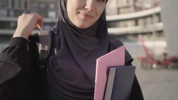 Mujer musulmana sonriente irreconocible en hiyab sosteniendo documentos y ajustando la mochila. Retrato de un estudiante feliz de Oriente Medio posando al aire libre en una ciudad soleada. Estilo de vida, educación, inteligencia . — Vídeos de Stock