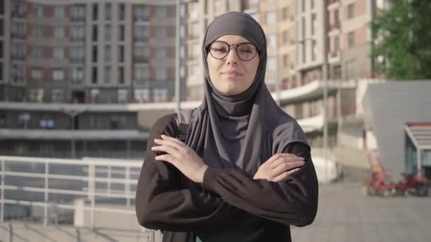 Confident smart muslim woman in hijab crossing hands and looking at camera. Portrait of positive beautiful Middle Eastern businesswoman posing outdoors with urban skyscraper at the background. — Stock Video