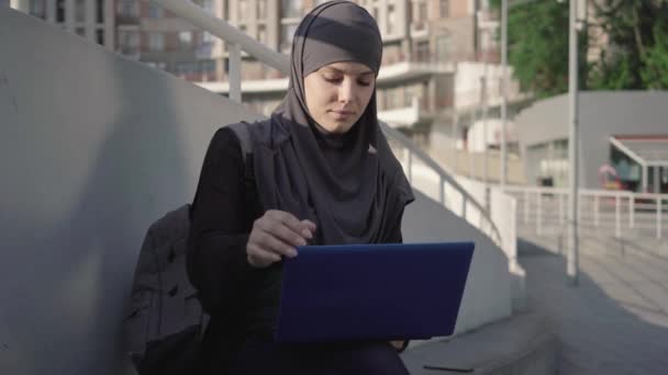 Retrato de jovem mulher concentrada no laptop de abertura hijab e digitação no teclado. Focada mulher de negócios do Oriente Médio surfar Internet ao ar livre na cidade. Comunicação sem fio, estilo de vida . — Vídeo de Stock