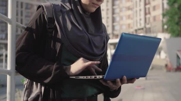 시내에 있는 노트북 키보드로 타이핑하는 히잡을 쓴 자신감 없는 젊은 여성. 바쁜 중동 여성 또는 학생 이 밖에서 인터넷 서핑을 하는 모습. 사업, 생활 방식, 교육. — 비디오