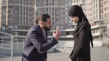 Orta Doğulu öfkeli bir adamın tesettürlü genç bir kadına bağırışının yan görüntüsü. Dışarıda karısına bağıran tatminsiz kocanın portresi. Aile içi şiddet, çatışma, ilişki sorunları, kıskançlık.
