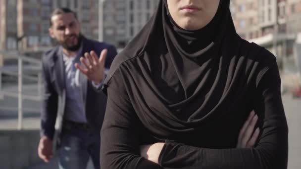 Mujer musulmana irreconocible con ropa tradicional de pie con las manos cruzadas como hombre enojado borroso gritando al fondo. Problemas de relación en la familia de Oriente Medio. Concepto de celos . — Vídeos de Stock