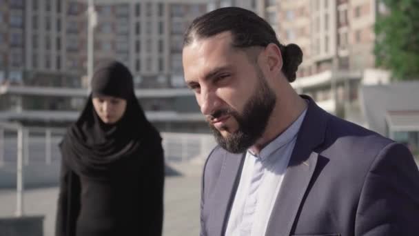 Primo piano volto di arrabbiato uomo del Medio Oriente guardando indietro a donna musulmana offuscata in hijab tradizionale e girando verso la fotocamera. Ritratto di marito geloso furioso insoddisfatto della moglie disobbediente. — Video Stock