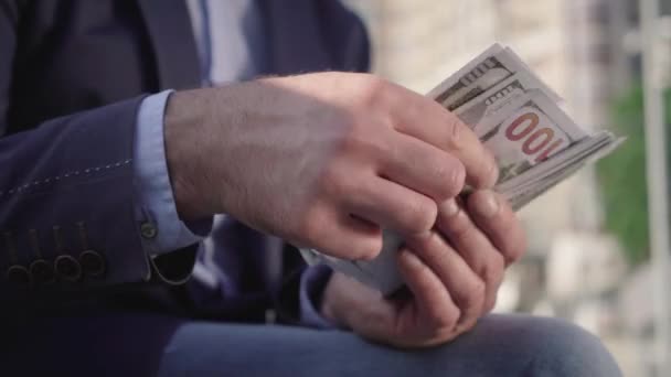 Close-up de mãos masculinas contando notas de dólar ao ar livre no dia ensolarado. Um homem rico irreconhecível a segurar um maço de dinheiro. Conceito de sucesso, riqueza, riqueza, negócio . — Vídeo de Stock