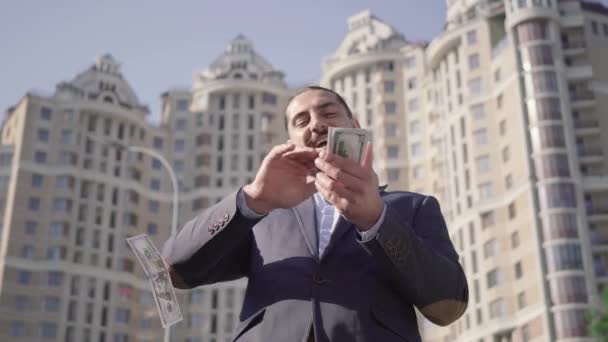 Boldog gazdag, sikeres ember szórja a pénzt a szabadban a felhőkarcoló hátterében. Portré elégedett közel-keleti üzletemberről, aki szórja a pénzt. Életmód, gazdagság, öröm, siker. — Stock videók