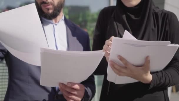 Selbstbewusste, bis zur Unkenntlichkeit unkenntliche Männer und Frauen aus dem Nahen Osten im Hijab, die an sonnigen Tagen im Freien Dokumente übergeben und miteinander reden. Professionelle Mitarbeiter diskutieren über Zusammenarbeit. Teamwork, Business, Lifestyle. — Stockvideo