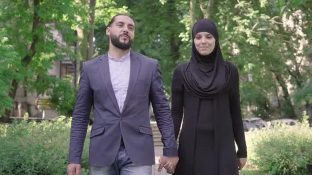 Portret van gelukkig liefhebbend echtpaar uit het Midden-Oosten wandelend in het zonnige zomerpark. Midden schot van lachende man met baard en jonge mooie vrouw in hijab die buiten loopt. Liefde, romantiek, verbinden. — Stockvideo