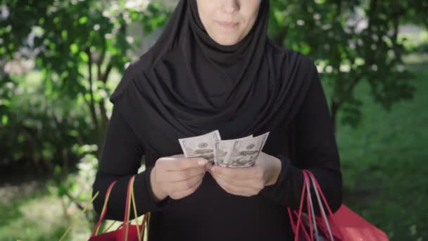 Femme méconnaissable en hijab comptant les billets et souriant. Jeune acheteur heureux du Moyen-Orient avec des sacs à provisions appréciant les achats à l'extérieur. Mode, shopaholism, style de vie, bonheur, succès. — Video