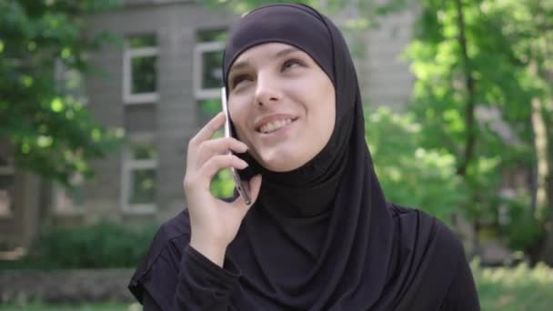 Зворотнє обличчя збудженої жінки-мусліма, яка розмовляє по телефону. Портрет веселої молодої дівчини з Близького Сходу за допомогою смартфона. Радість, спосіб життя, спілкування. — стокове відео