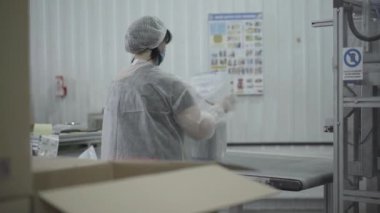 Kafkasyalı kadının üretim hattında hazır yemek kapları paketlediği arka plan görüntüsü. Otomatik makinenin yanında çalışan koruyucu üniformalı profesyonel kadın çalışan. Endüstri, üretim.