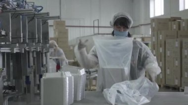 Covid-19 salgını sırasında fabrikada çalışan maskeli beyaz kadınlar. Üretim alanında bitmiş ürünleri taşıyan kadın çalışanların portresi. Sanayi, iş.
