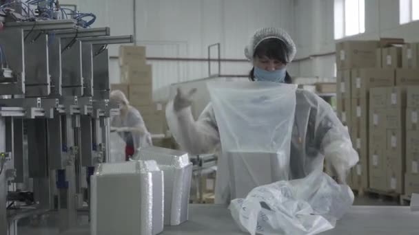 Mujeres caucásicas con máscaras faciales trabajando en fábrica durante la pandemia de Covid-19. Retrato de empleadas empacando productos terminados en el transportador en el sitio de fabricación. Industria, negocios . — Vídeos de Stock