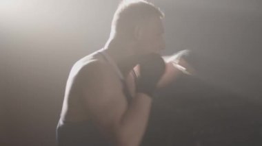 Kafkasyalı boksörün arka planda antrenman yapışının yan görüntüsü. Sis içindeki karanlıkta kendine güvenen sporcu boks gölgesi. Dövüş sanatları konsepti, spor, güç, erkeklik. Sinema 4k ProRes Merkezi.