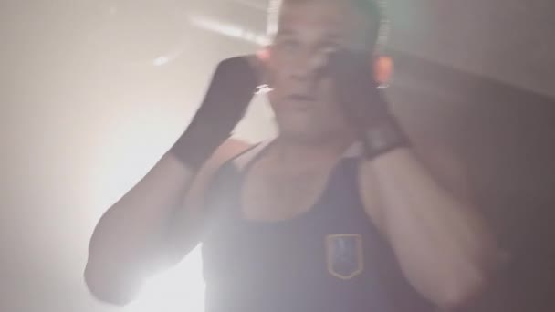 Живая камера показывает молодого спортсмена, движущегося в линзовой вспышке в тумане. Портрет уверенного кавказского боксера, пробивающего воздух в туманном спортзале. Красавчик тренируется в подсветке. Штаб-квартира кинотеатра 4k ProRes . — стоковое видео