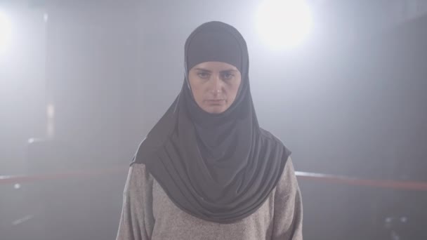 Mladá sebevědomá muslimka v hidžábu se dívá na kameru a zvedá ruce v boxerských rukavicích. Portrét krásné boxerky pózující v oparu v podsvícení. Sebevědomí, životní styl. Cinema 4k ProRes HQ. — Stock video