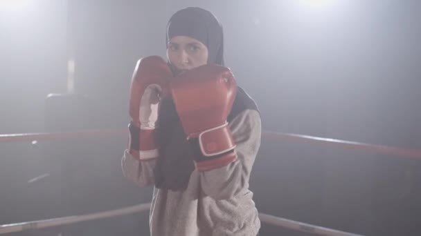 Hermosa boxeadora musulmana en hijab luchando con cámara en vivo en slow mo. Retrato de una joven entrenando en el ring de boxeo en niebla con retroiluminación en el fondo. En cámara lenta. Sede del cine 4k ProRes . — Vídeos de Stock