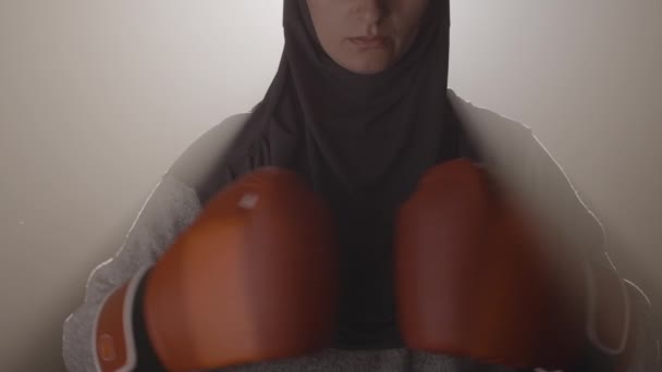 有信心的穆斯林女拳击手的特写，戴着拳击手套，看着镜头。漂亮而严肃的女运动员在雾蒙蒙的背光中摆姿势.摄像头向上移动。Cinema 4k ProRes HQ. — 图库视频影像