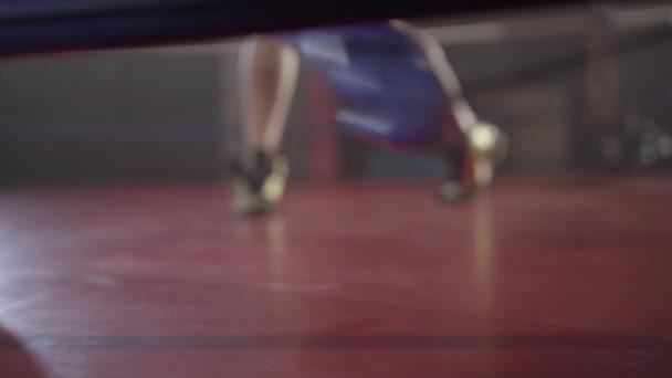 Close-up van een bokser die op een boksring valt. Portret van een jonge blanke sportman die verliest. Voeten van wazige man op de achtergrond. Sparen, vechtsport, vechtsport, levensstijl. — Stockvideo