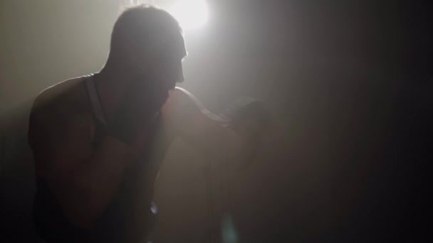 Sylwetka człowieka walczącego z cieniem w podświetleniu. Widok z boku młodego, silnego, białego boksera bijącego powietrze w mgle. Sztuka walki, sport walki, trening, trening. — Wideo stockowe