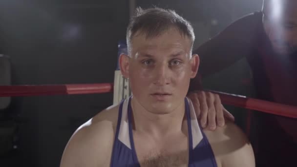 Entraîneur endossant jeune boxeur transpirant assis dans le coin du ring de boxe. Caméra approche du visage en colère du sportif caucasien prêt pour le combat. Sport de combat, compétition, championnat. — Video