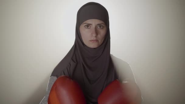 Kameran närmar sig den vackra ansiktet av allvarliga muslimska kvinna i hijab i dimmiga bakgrundsbelysning. Självsäker brunögd boxare som poserar i dis med lins. Idrott, kampsport, jämställdhet. — Stockvideo