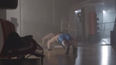 Spor salonunda şınav çeken güçlü bir boksör. Aynanın önünde kendine güvenen beyaz tenli sporcuların antrenmanlarının arka planında. Spor, yaşam tarzı, dövüş sanatları. Sinema 4k ProRes Merkezi.