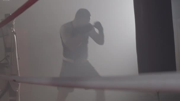 广谱拍摄的健康自信的高加索拳击手在拳击台上打拳袋.年轻的运动员在雾蒙蒙的体育馆里活动.武术，格斗运动。现场摄像头。Cinema 4k ProRes HQ. — 图库视频影像