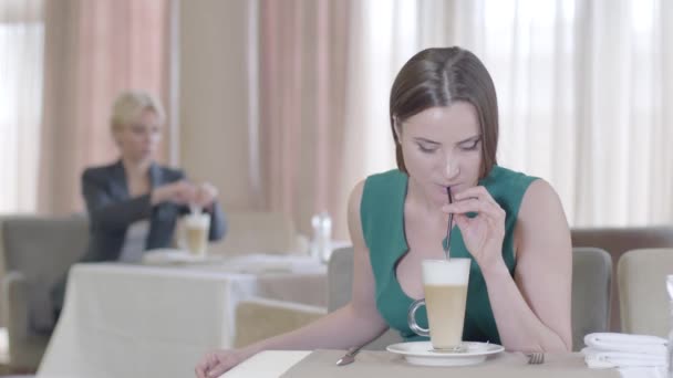 Prachtige brunette vrouw proeven heerlijke latte of cappuccino in cafe. Portret van een mooie glimlachende blanke dame met groene ogen die koffie drinkt in restaurant. Vreugde, vrije tijd, levensstijl. — Stockvideo