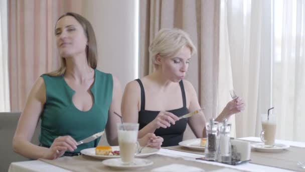 Brünette Kaukasierin im Gespräch mit einem blonden Freund, der leckeres Dessert isst. Junge Frauen essen im Restaurant und unterhalten sich. Lebensstil, Pause, Erholung, Freizeit. — Stockvideo