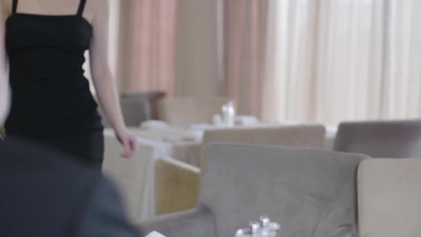 Elegante blonde blanke vrouw in zwarte jurk te laat voor de date. Portret van een mooie zelfverzekerde dame die naar de tafel komt in het restaurant en zich verontschuldigt voor niet-stiptheid. Afspraakjes, levensstijl. — Stockvideo